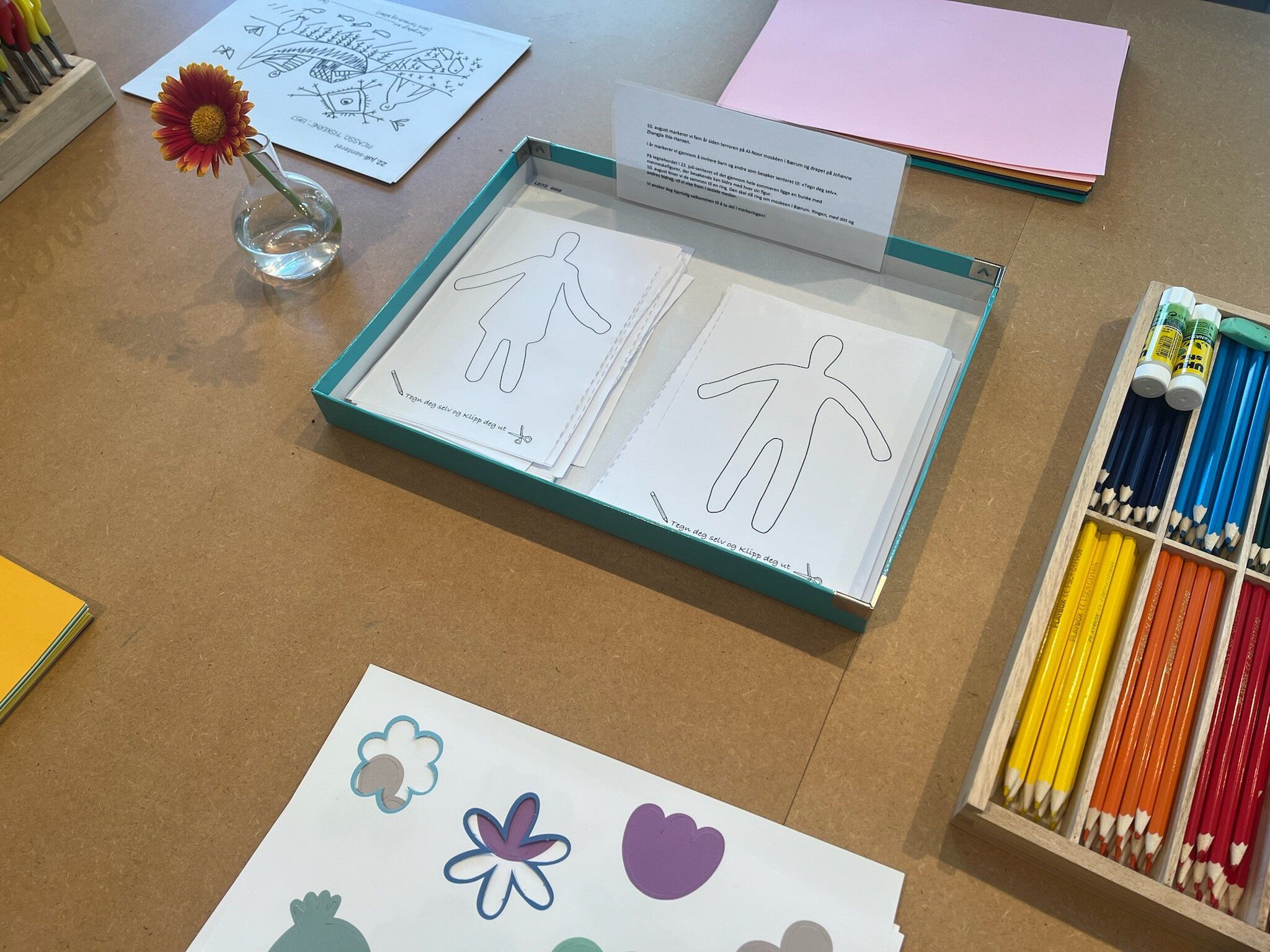 Close up of a table with paper, pencils and a flower in a vase.