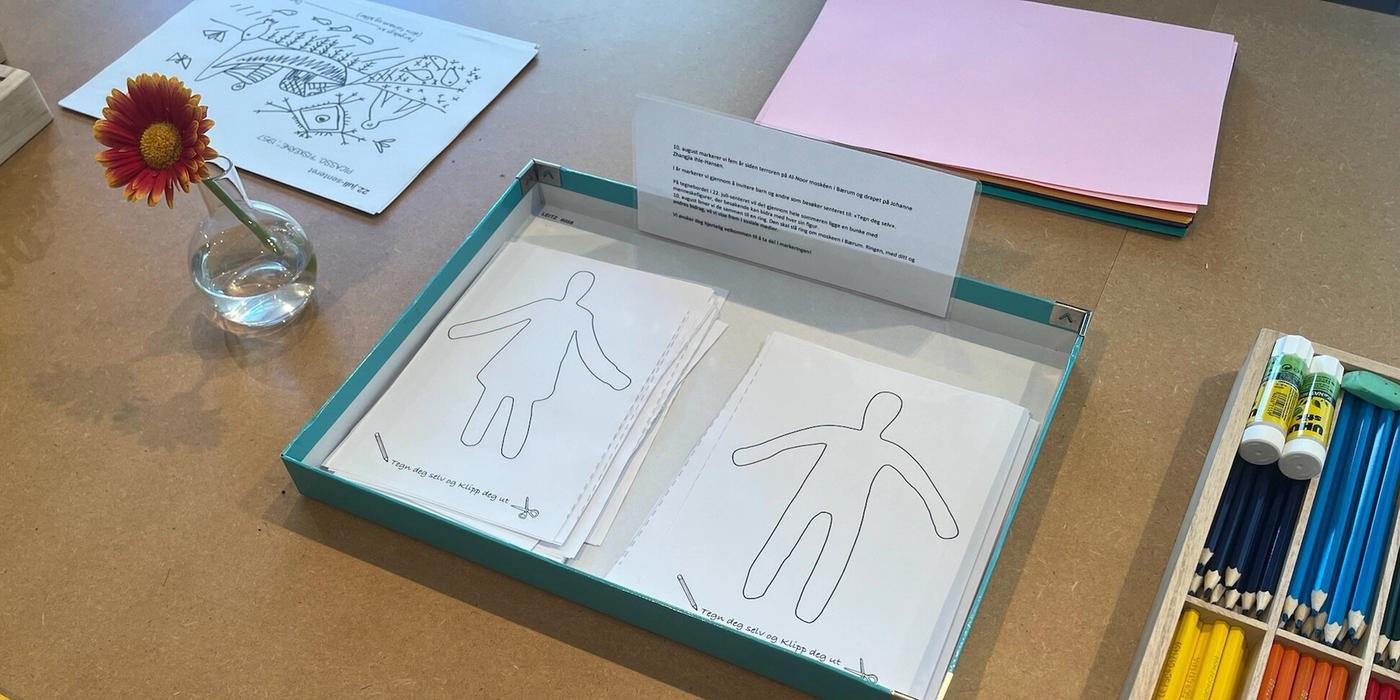 Nærbilde av et bord med ark, blyantstifter og en blomst i vase.