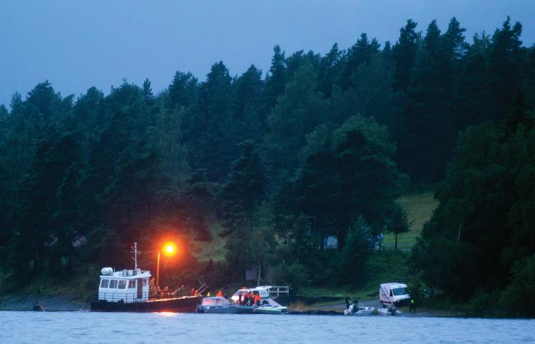 Water in the foreground. Ferry. Unknown number of people. A car. Forest. In the dusk. 