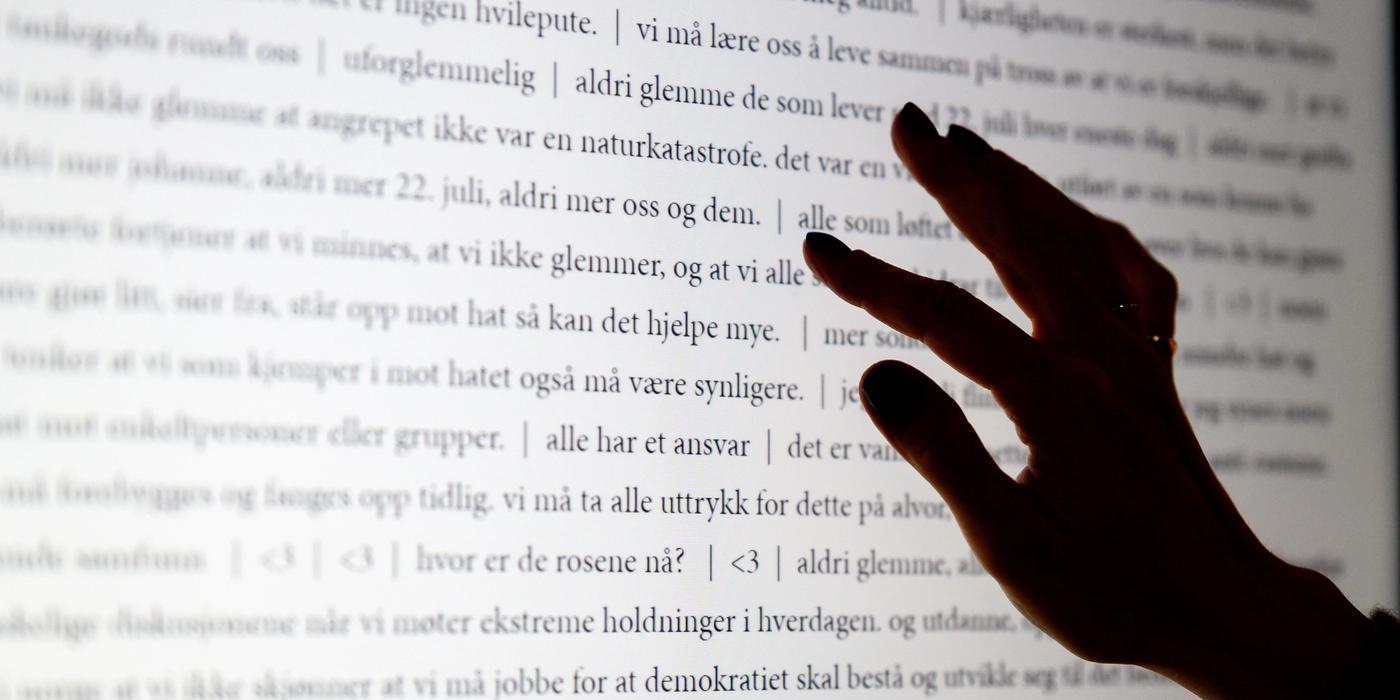 A hand on a screen with text. From the text that is in focus, one can read "July 22, never more us and them."