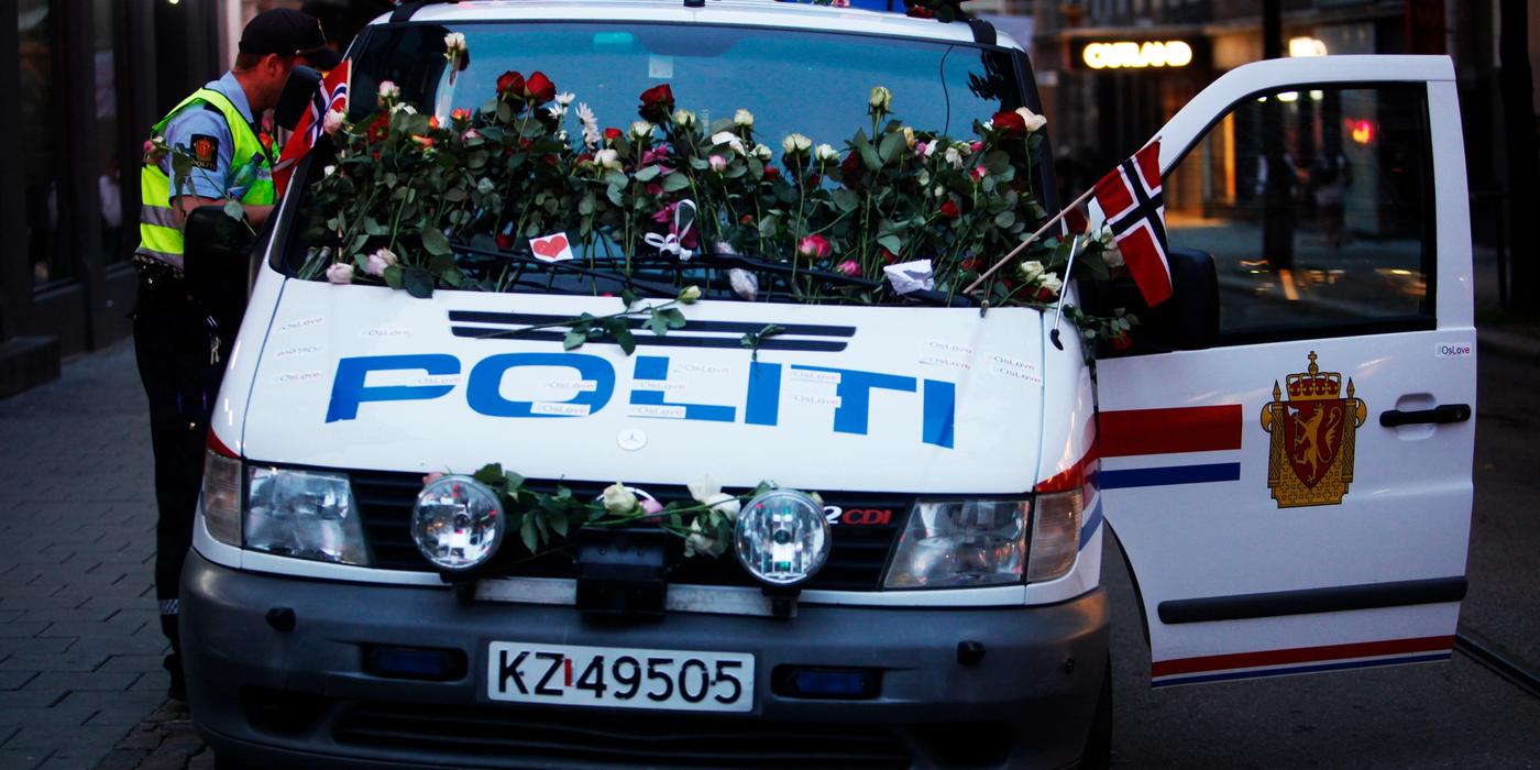 Politibil dekket med blomster og flagg. En politimann står i uniform ved bilen. Foto