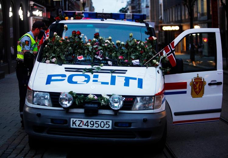 Police car covered in flowers and flags. A policeman in uniform stands by the car. Photo