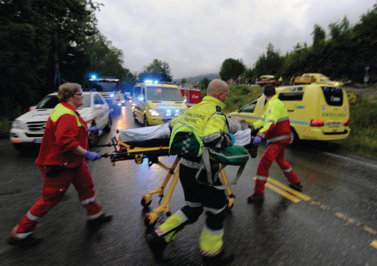  Three people transfers a stretcher with an injured camp participant. Two cars with sirens. Two cars. Several cars in the background in the picture.