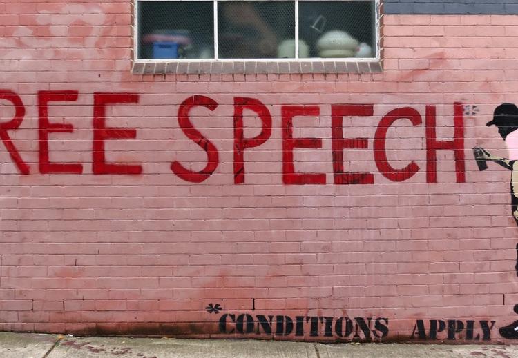 Street art med bilde av av en person som tagger teksten "Free speech" på rosa bakgunn. Det står tekst: "Conditions Apply". 