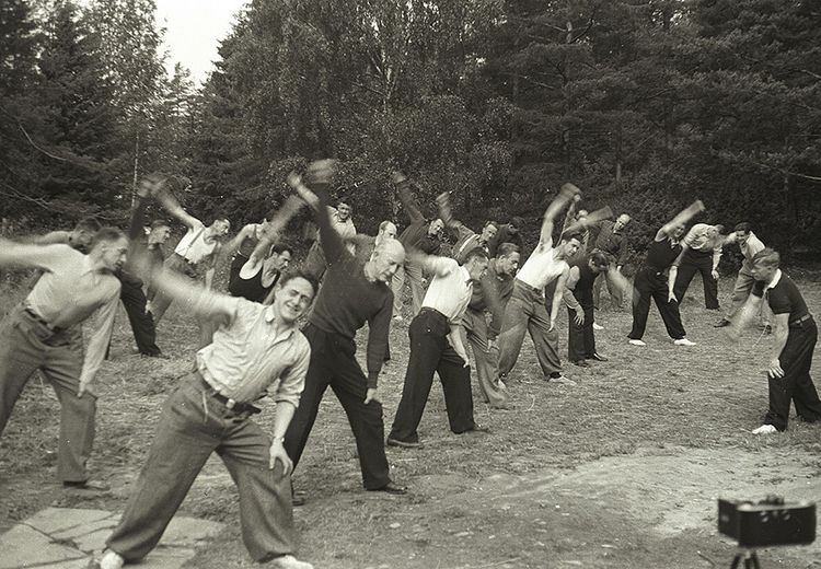 Bilde i sort og hvit av en gruppe av ca. 25 menn trener i en skoglysning.