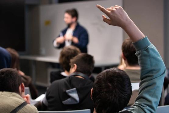 In the foreground: a student raising his hand. in the background a teacher.