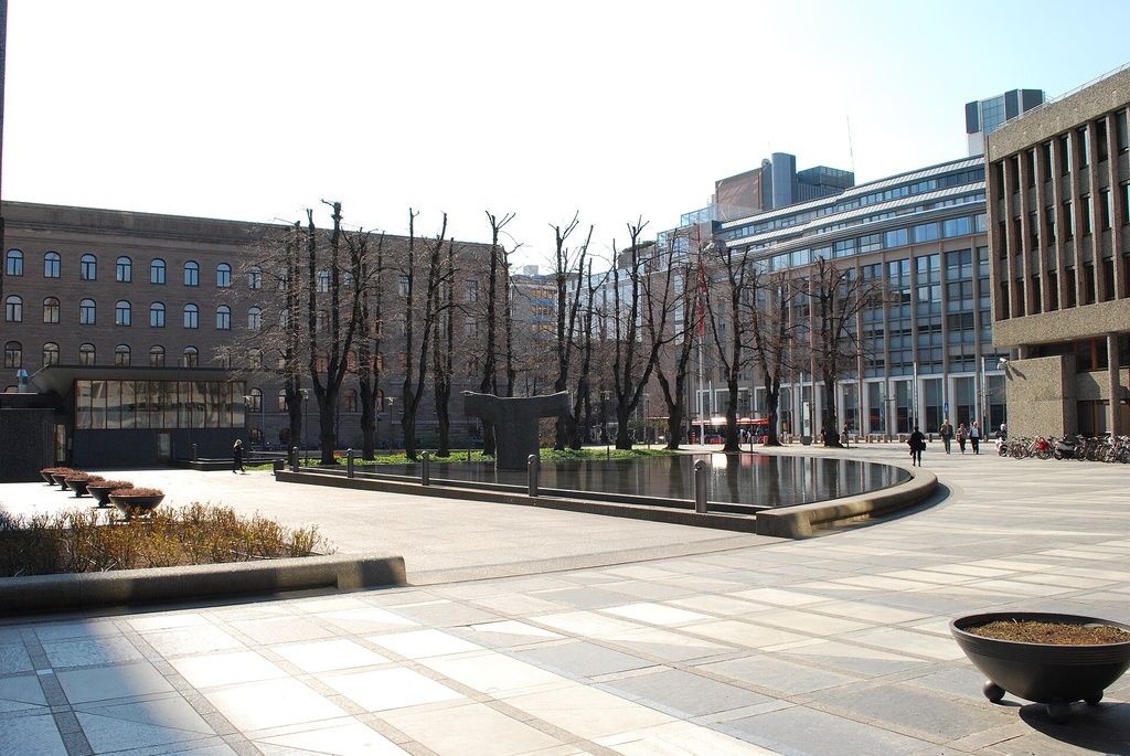 Place with a water pool, large building. Sculpture. Trees.