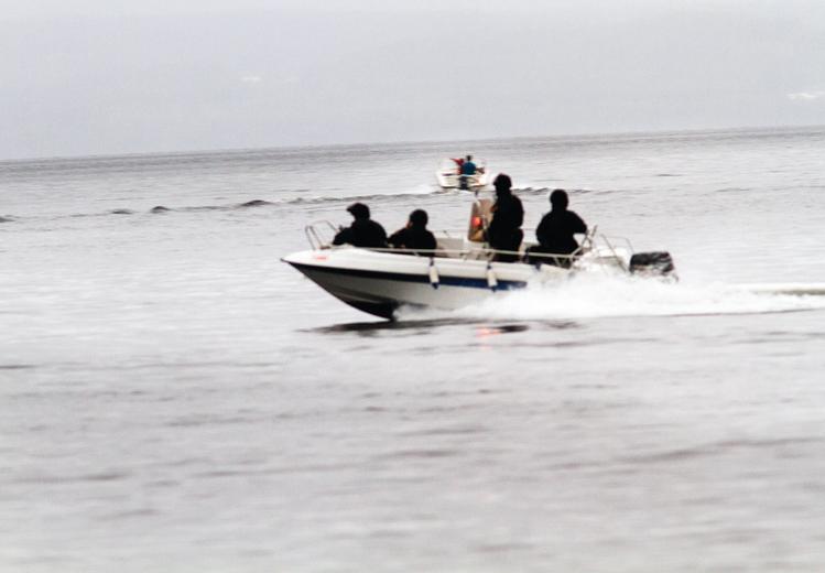 Vann. En båt med fire mennesker i uniform i forkant. En båt i bakgrunnen.