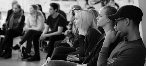  Black and white picture. Pupils sitting in a group. Three students in profile in the foreground, several students in the background.