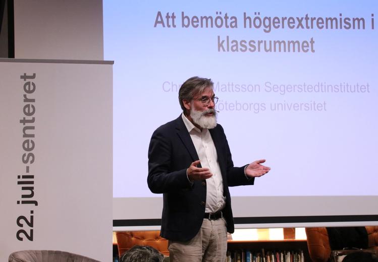 En mann med skjegg snakker foran en stor skjerm hvor man kan lese "Att bemöta högerextremism i  klassrummet". Til venstre av skjermen en roll-up med 22. juli-senterets logo. 