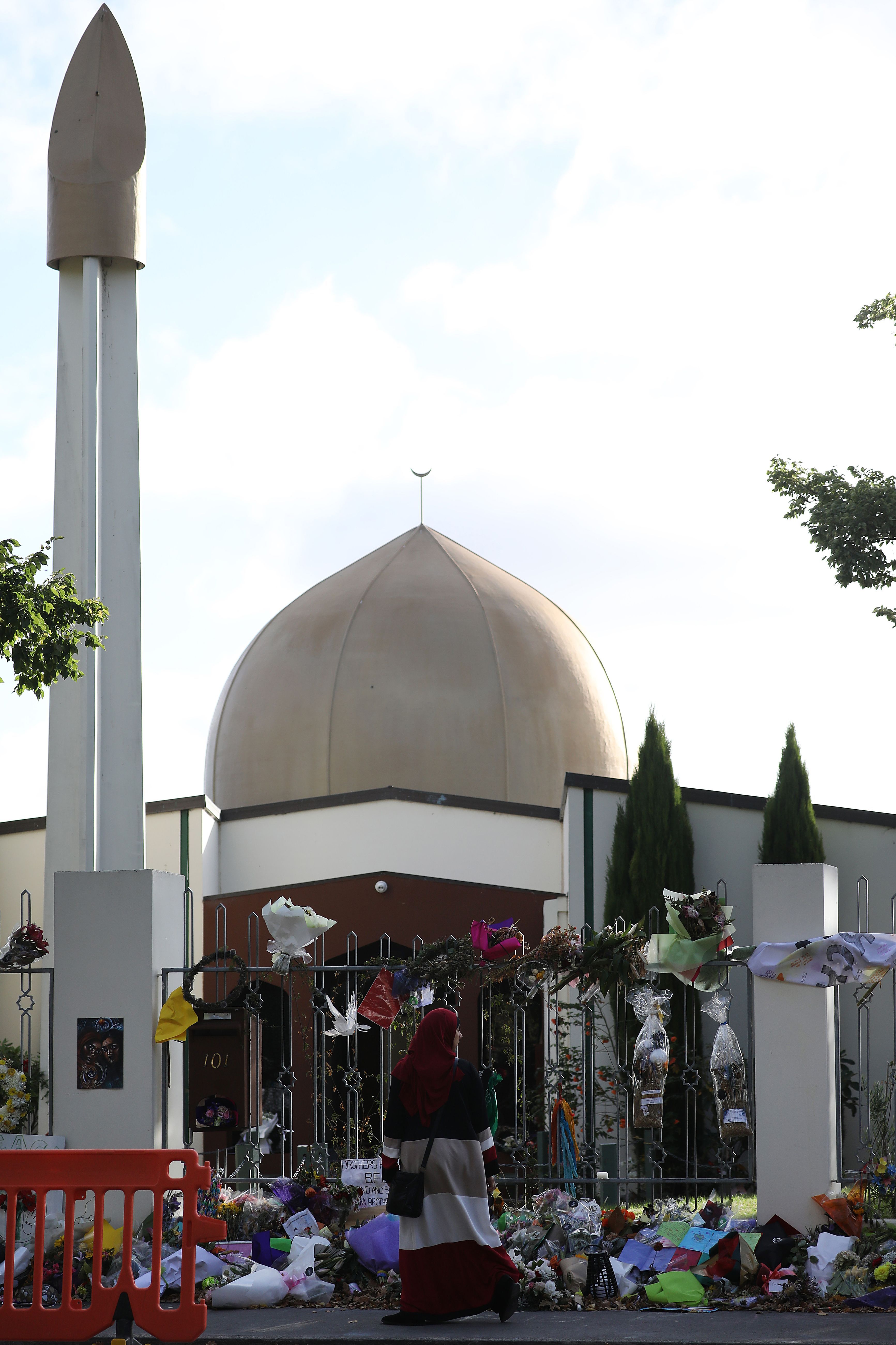 Red barrier in front of a crowd. Mosque in white with a tall tower. Brown/grey dome.