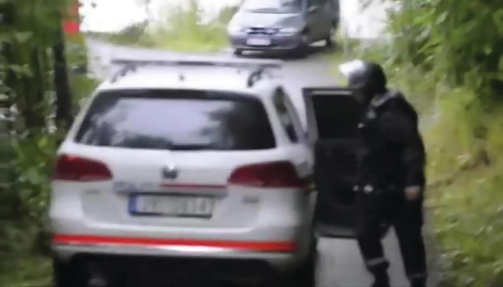 Blurry screenshot from video recording. A uniformed person with a helmet and black clothes opens a white car. 