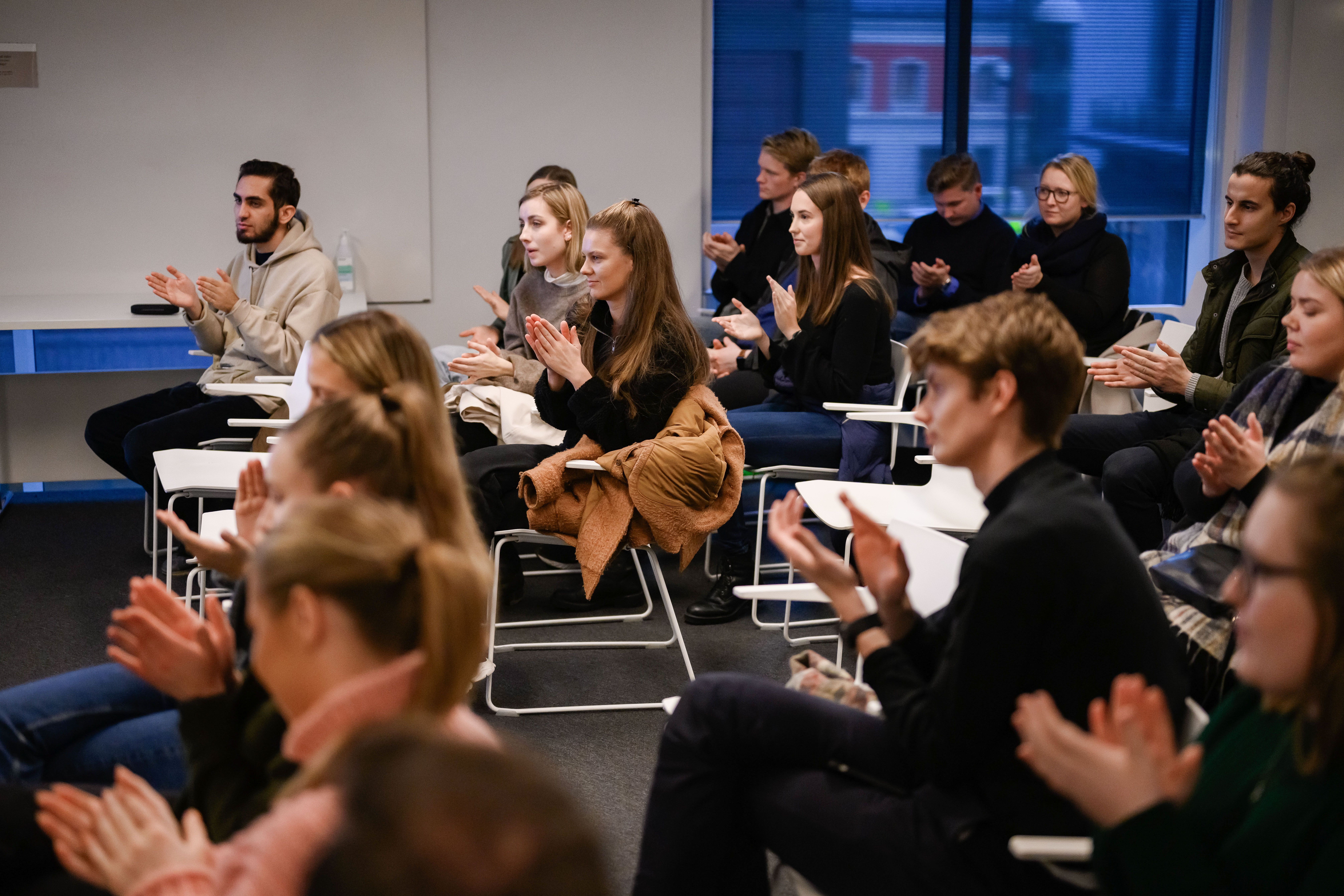 En gruppe mennesker sitter på hvite stoler og applauderer. 