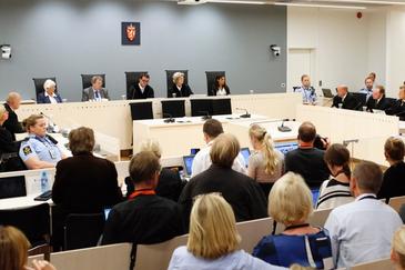 Bilde av et lokale hvor en rettssak foregår. Flere formelt kledde mennesker, to personer i rettskappe og fire politibetjenter. Foto