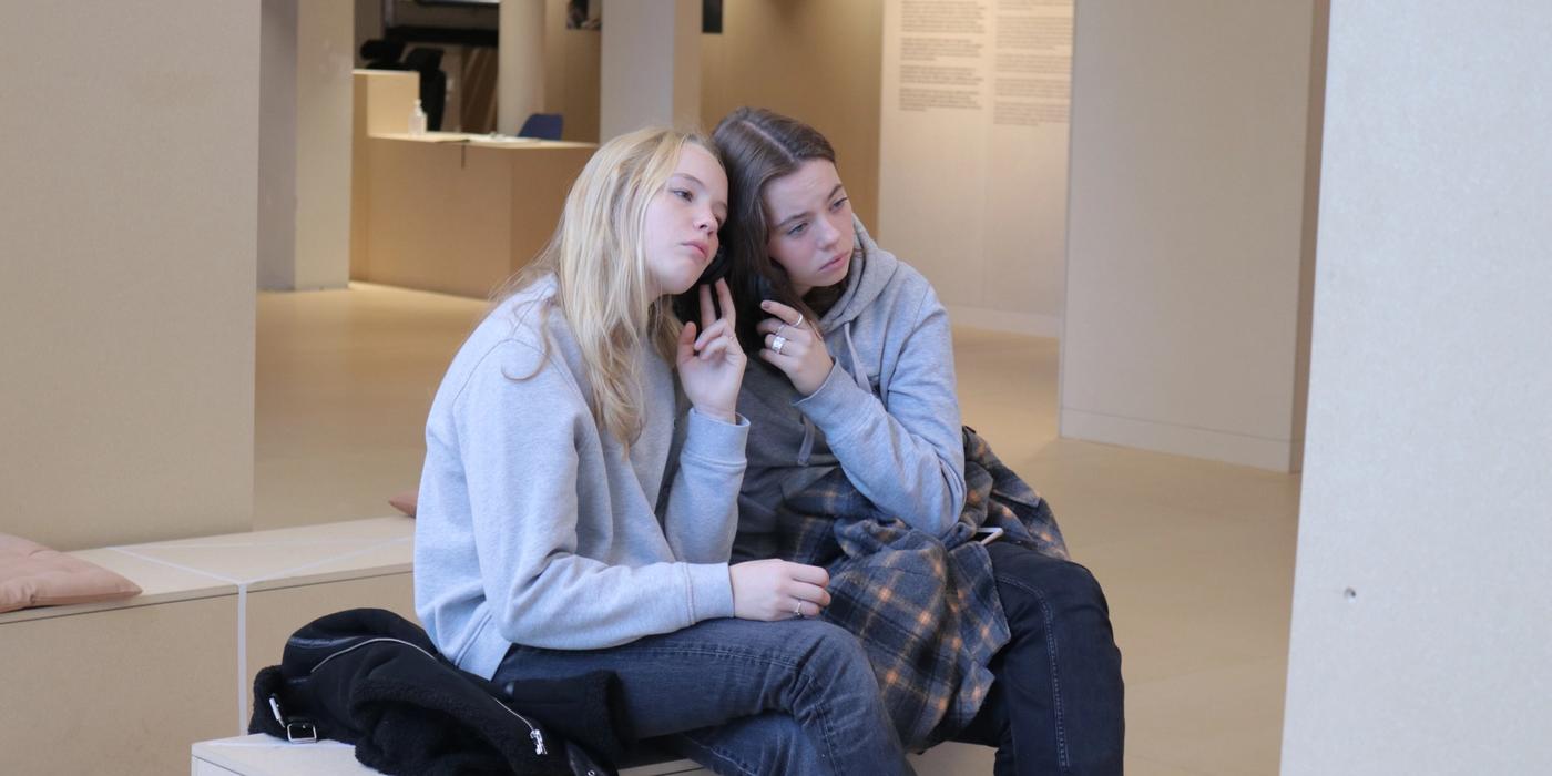 Two girls sitting share headphones.