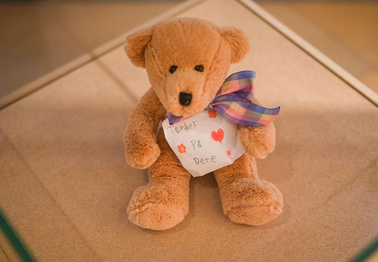 Teddy bear in exhibition display. The teddy bear has a bow around its neck and a note with the words "thinking of you" written.
