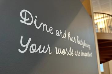 Nærbilde av grå vegg med hvit foliert skrift i løkke med teksten: Dine ord har betydning