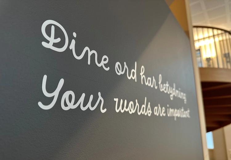 Nærbilde av grå vegg med hvit foliert skrift i løkke med teksten: Dine ord har betydning