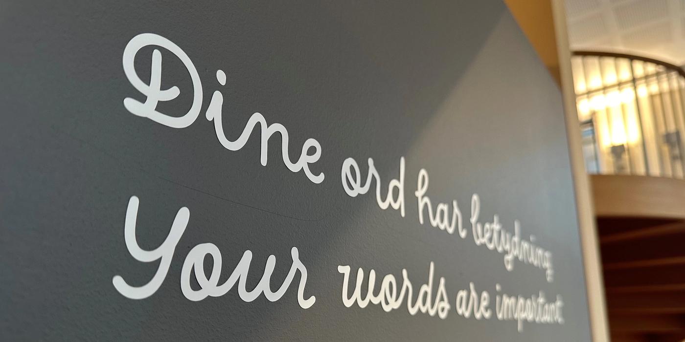 Nærbilde av grå vegg med hvit foliert skrift i løkke med teksten: Dine ord har betydning