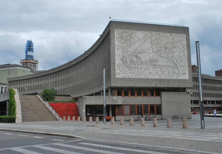 Lang lavt bygg. Betong kunst på enden av bygget. På kunsten er det en sol, garn og mennesker som fisker.