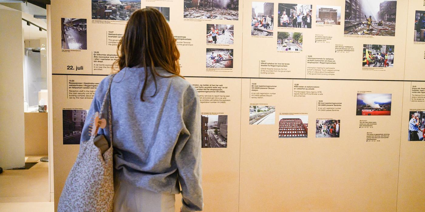 A woman with jeans and a tote bag is looking at at timeline with pictures and texts in an exhibition room.