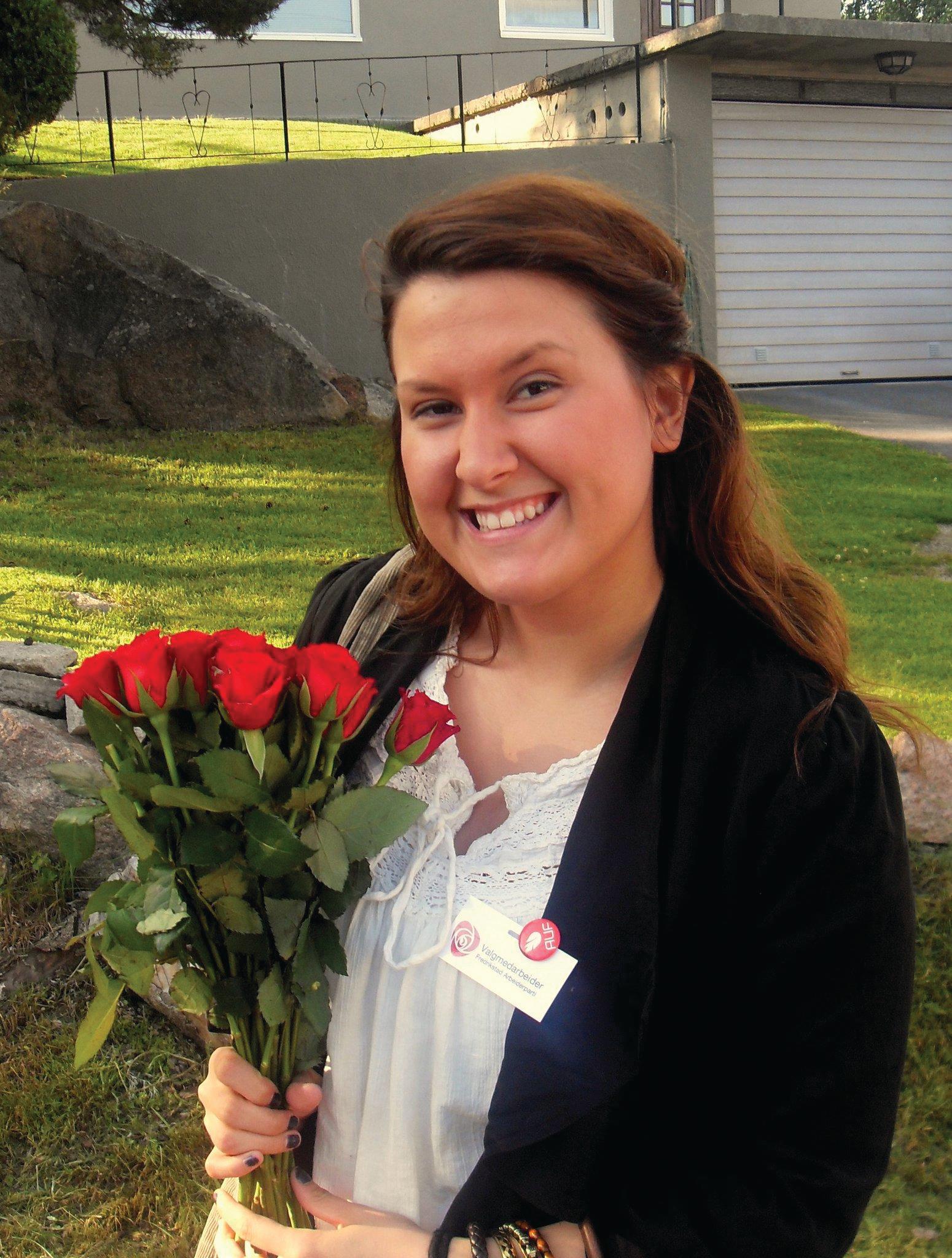 Bilde av en smilende jente med roser i hendene. Nærbilde. Plen og hus i bakgrunnen