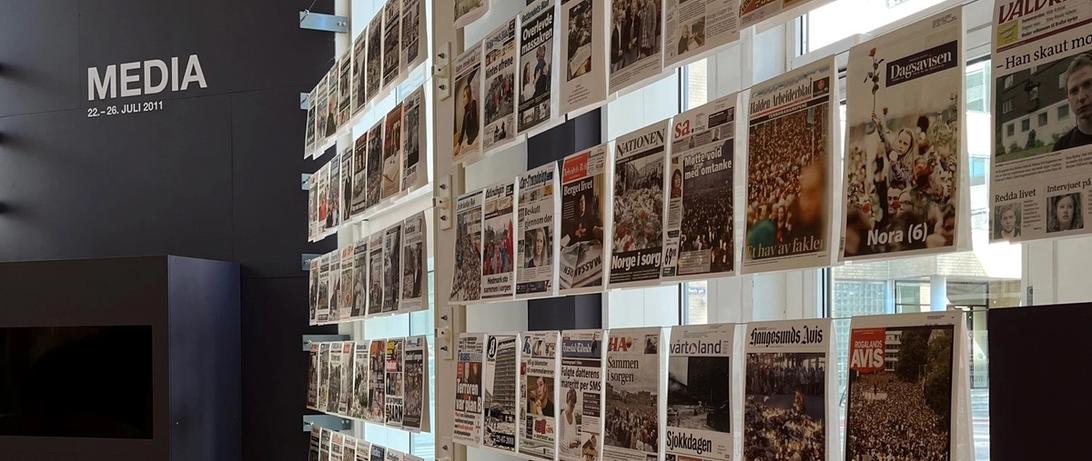 Flere avisforsider utstilt i 22. juli-senterets lokaler. Media står skrevet i stor skrift i bakgrunnen.
