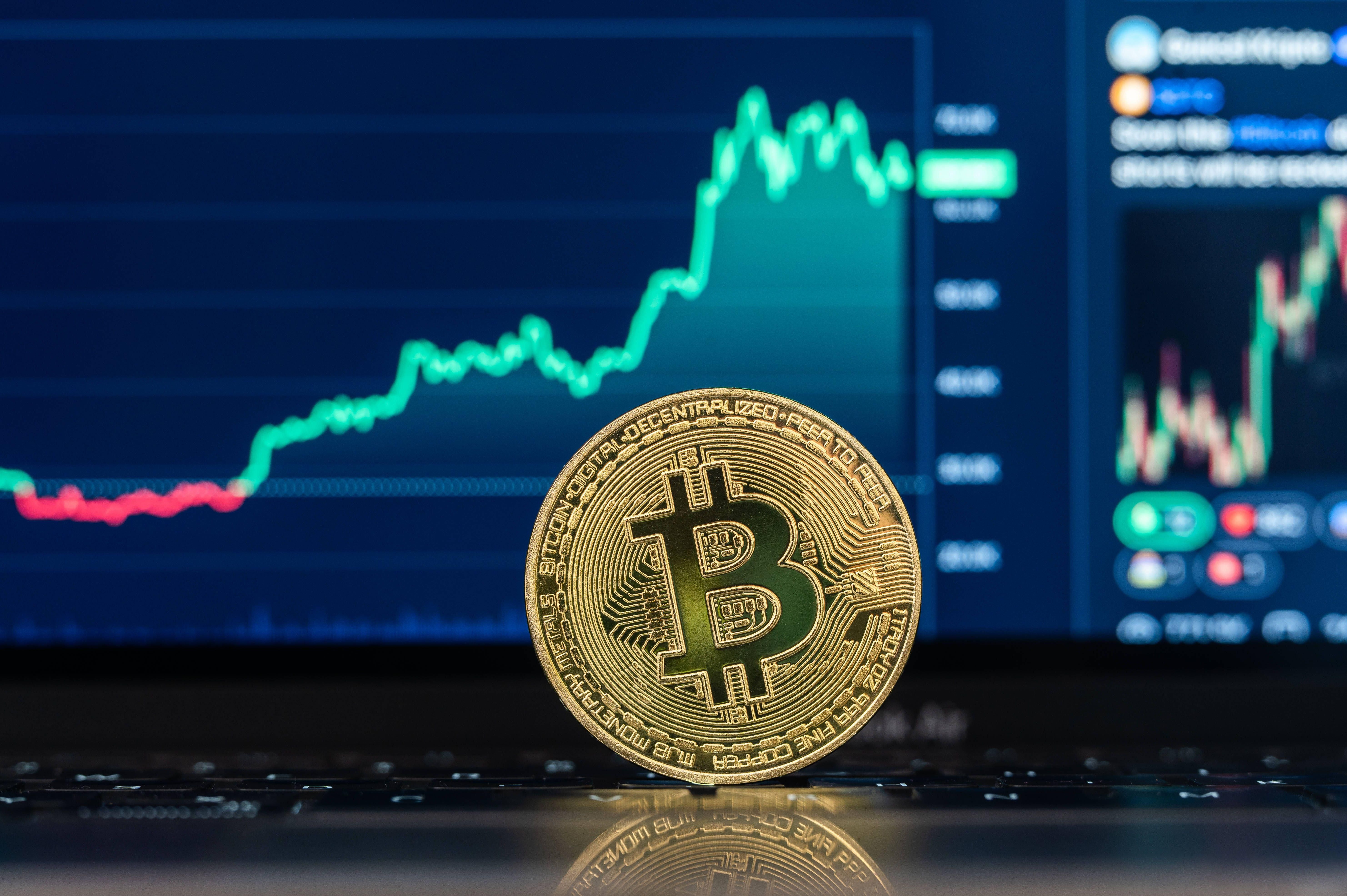 The logo of Bitcoin can be seen on a coin standing in front of a Bitcoin chart of the trading platform CoinMarcetCap