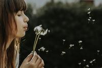 Woman blowing dandelion seeds in wind