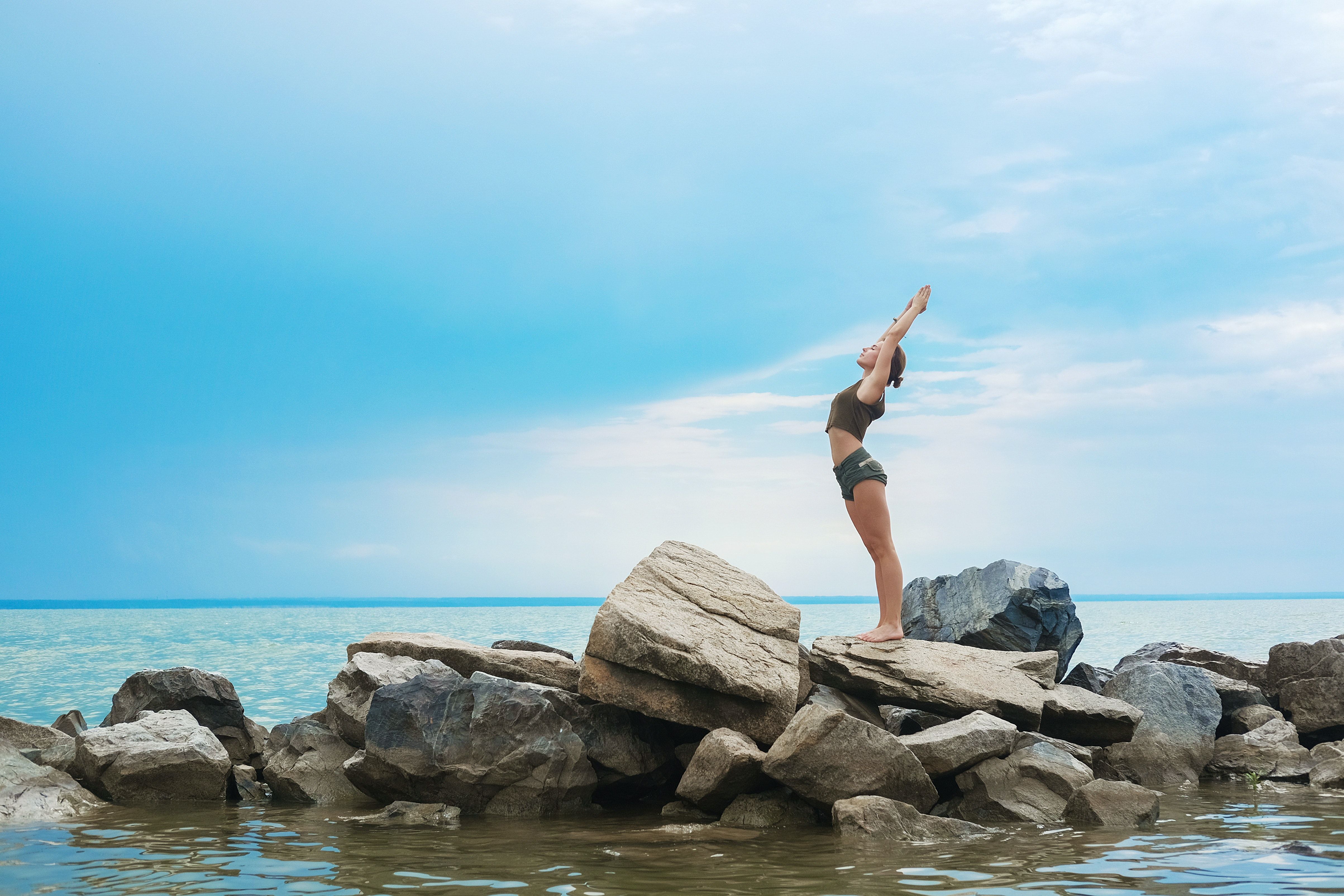 woman on rocks in sea reaching for sky