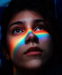 Woman looking up with rainbow prism going over nose