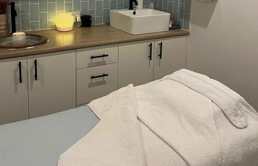 Prepared treatment bed beside a tiled sink and warm lamp