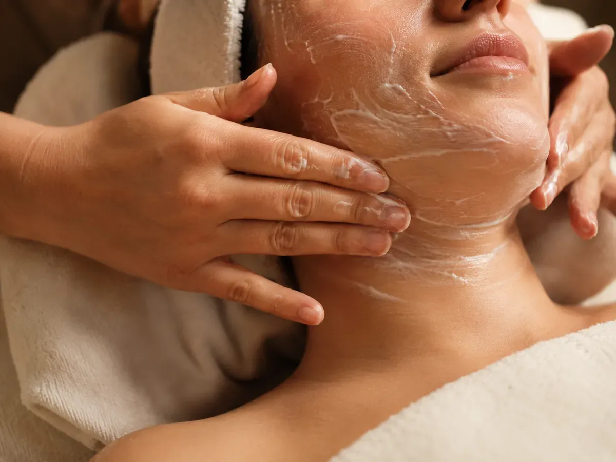 Facial treatment with cream cleanser being massaged into the cheek and jaw