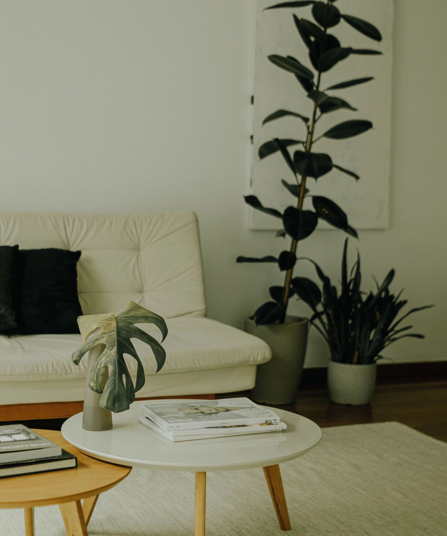 A calm living room in cream and natural tones with large indoor plants beside the window