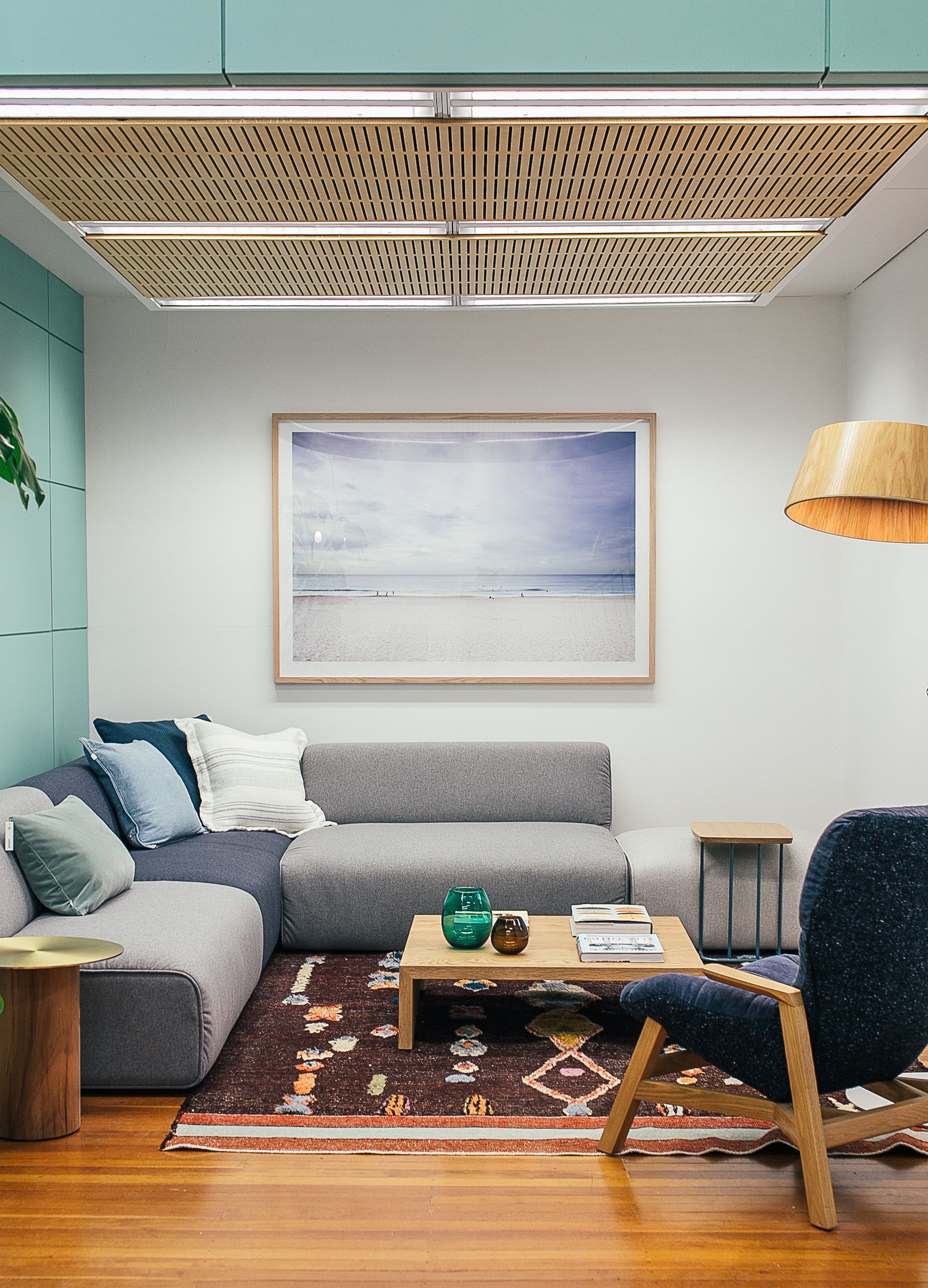 A living room with a low grey sofa, warm timber and a framed coastal print