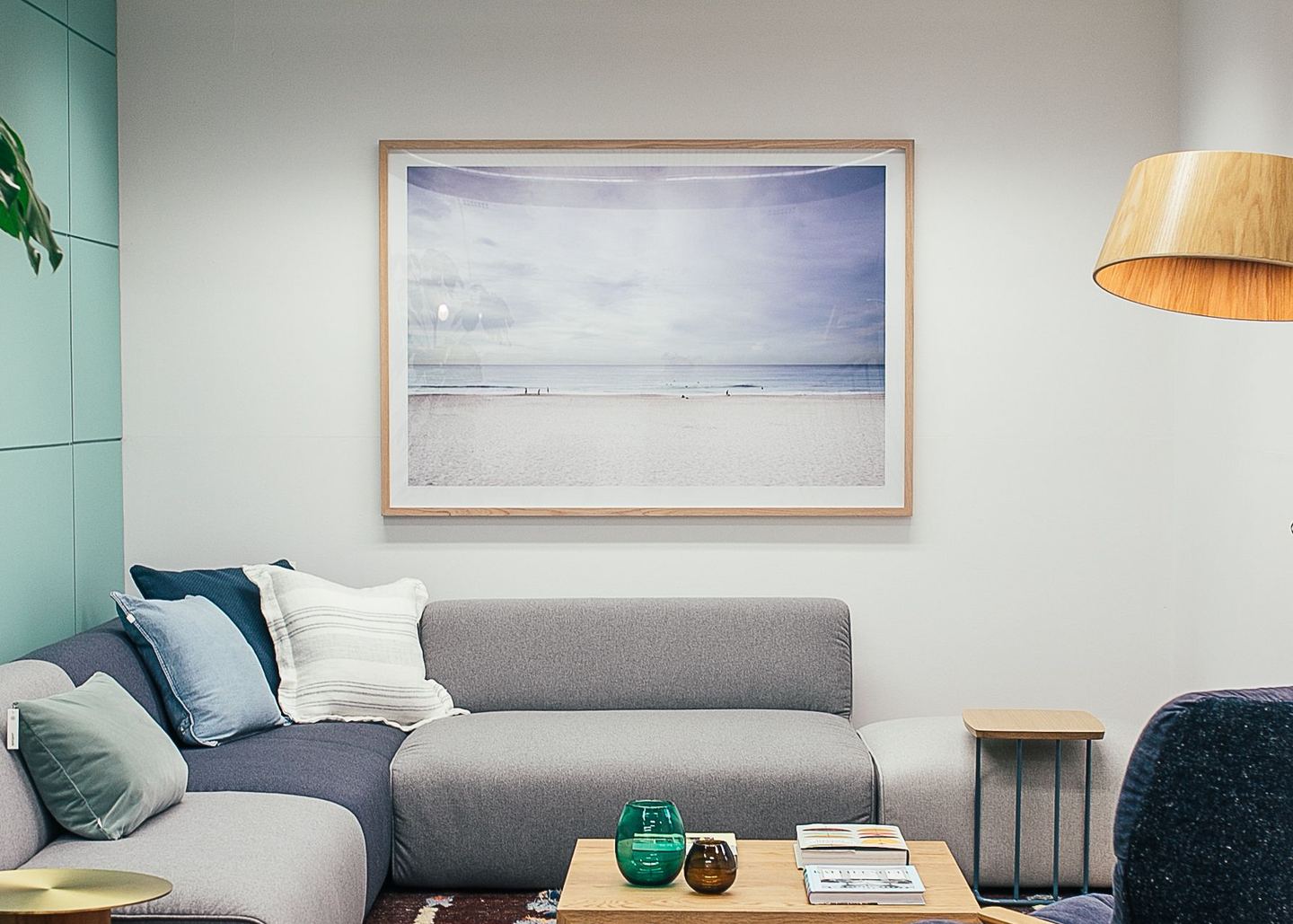 A living room with a low grey sofa, warm timber and a framed coastal print