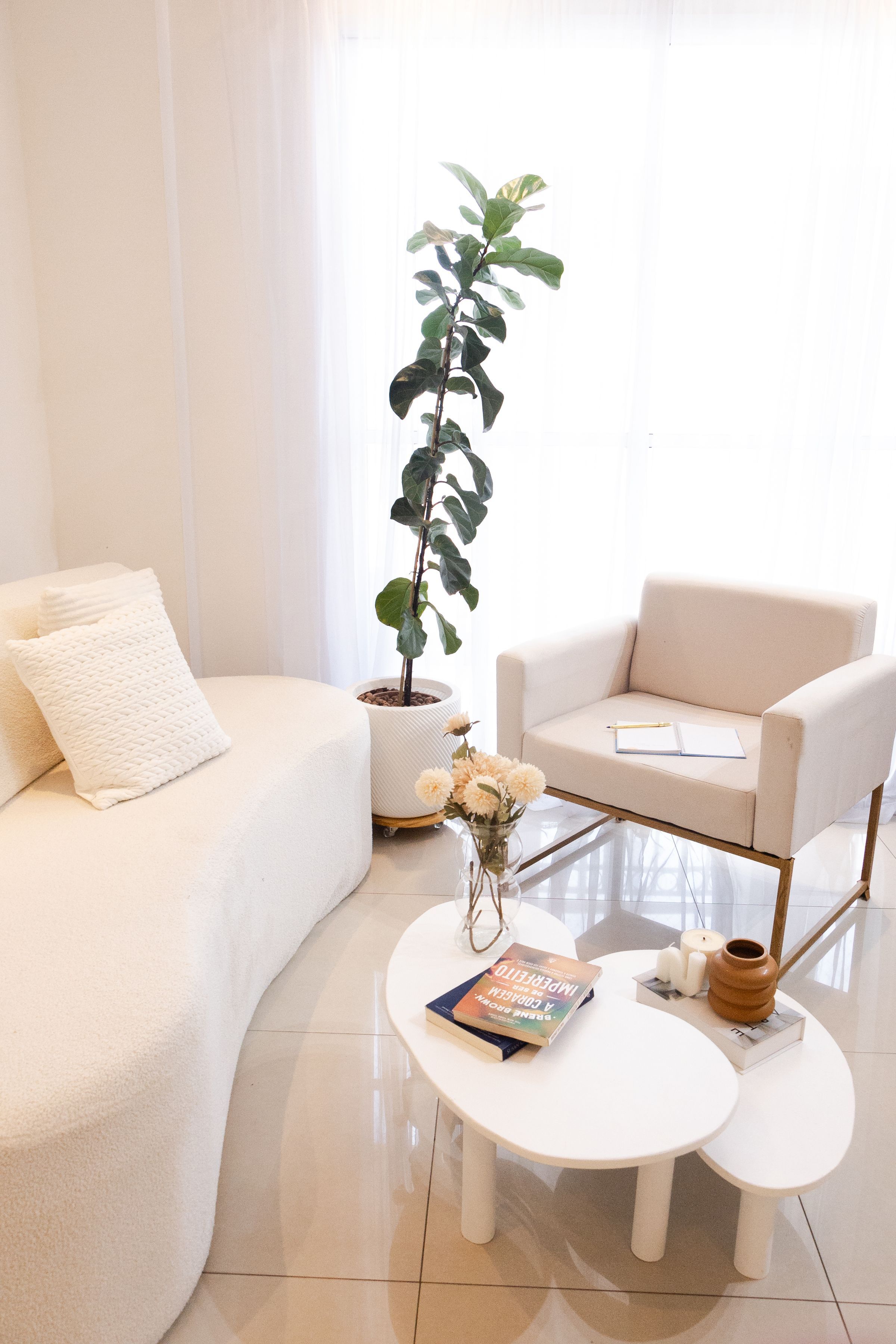 A pale, airy sitting room with white upholstery and a potted fig