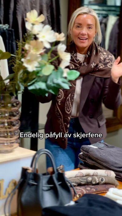 Kvinne med mønstret skjerf i butikken, vesker i forgrunnen