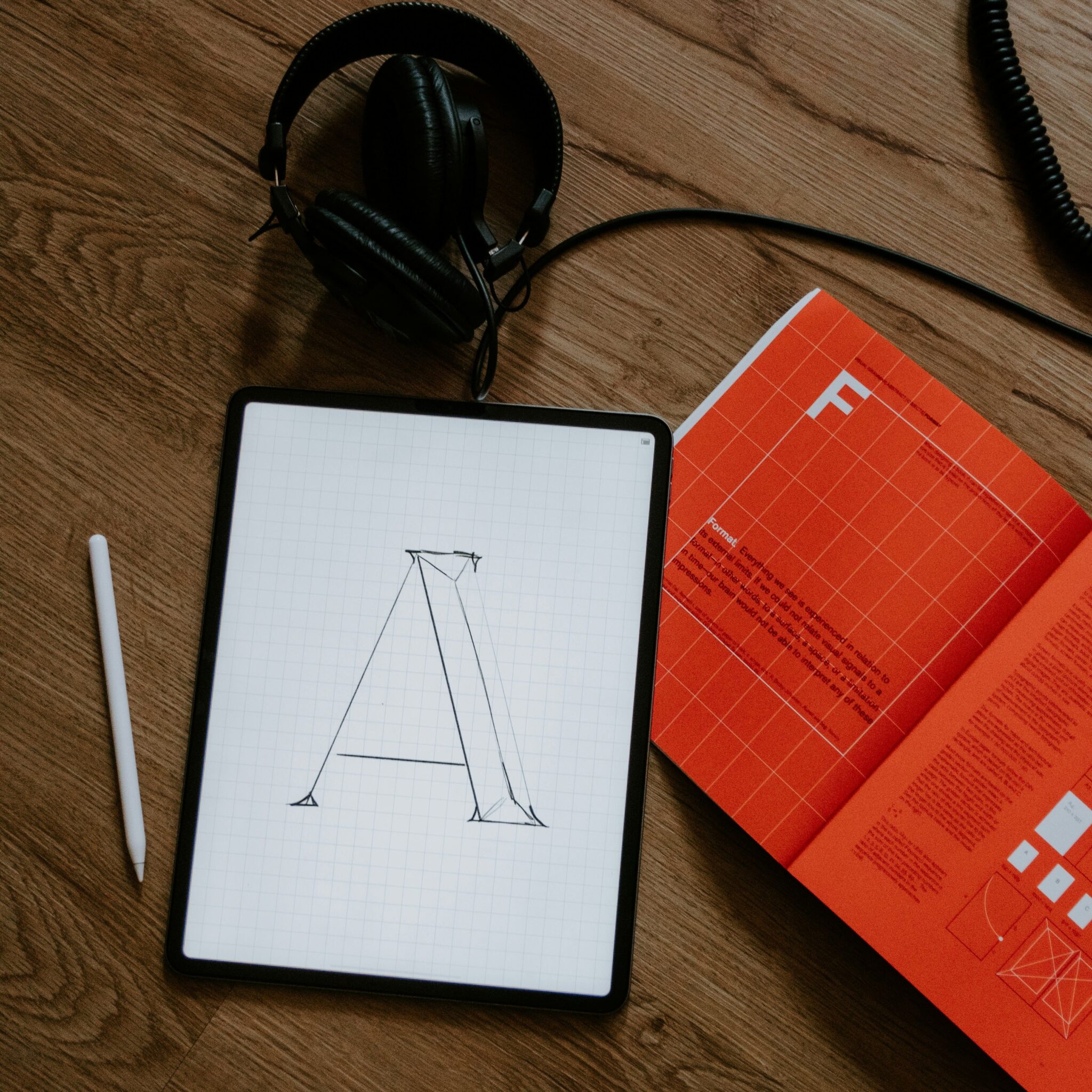Letter A sketched on a tablet beside a type specimen book and headphones