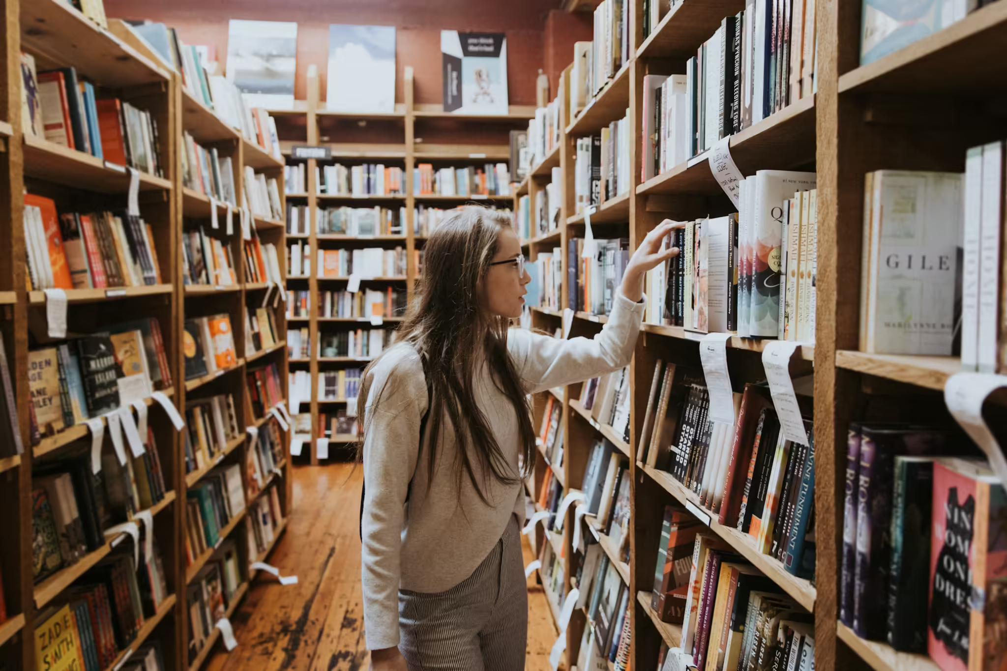 Student browsing shelves in a library between tall rows of books