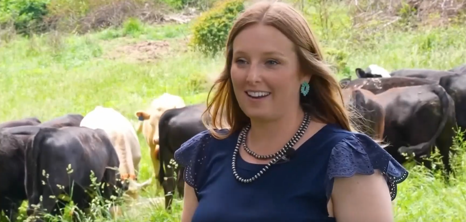 Deidre Tigue talks with an RFDTV reporter with cattle in the background wearing eShepherd neckbands