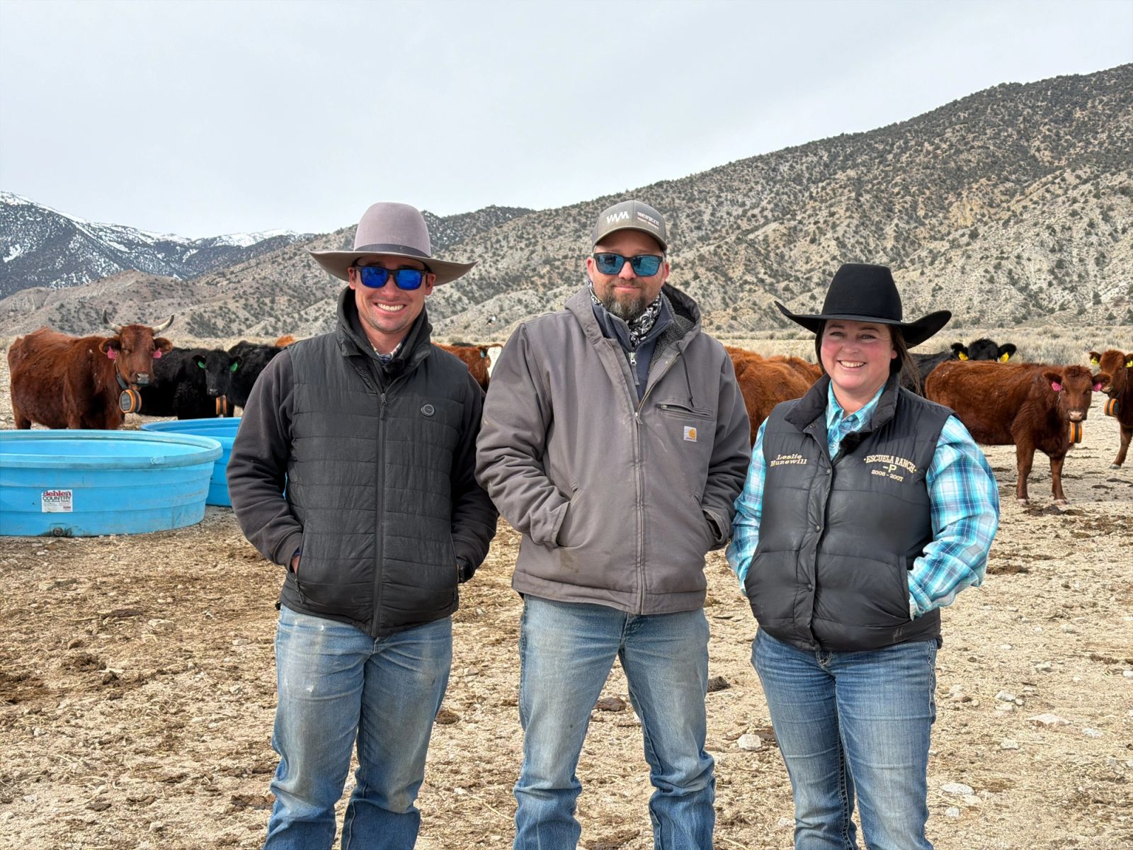 Dalton Wright, Blair Hunewill, and Leslie Hunewill stand in front of a watering point with cattle in the background