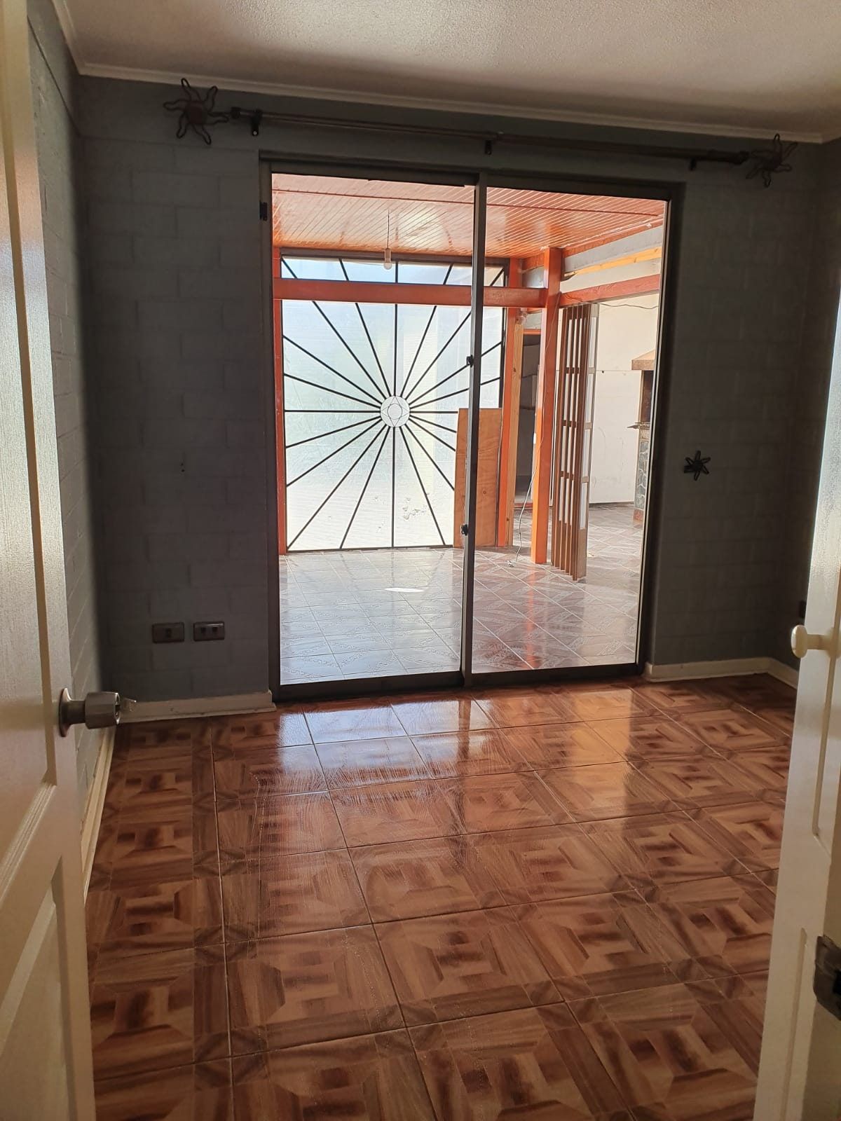 Habitación con piso cerámico diseño parquet y ventanal de acceso al patio con reja metálica.