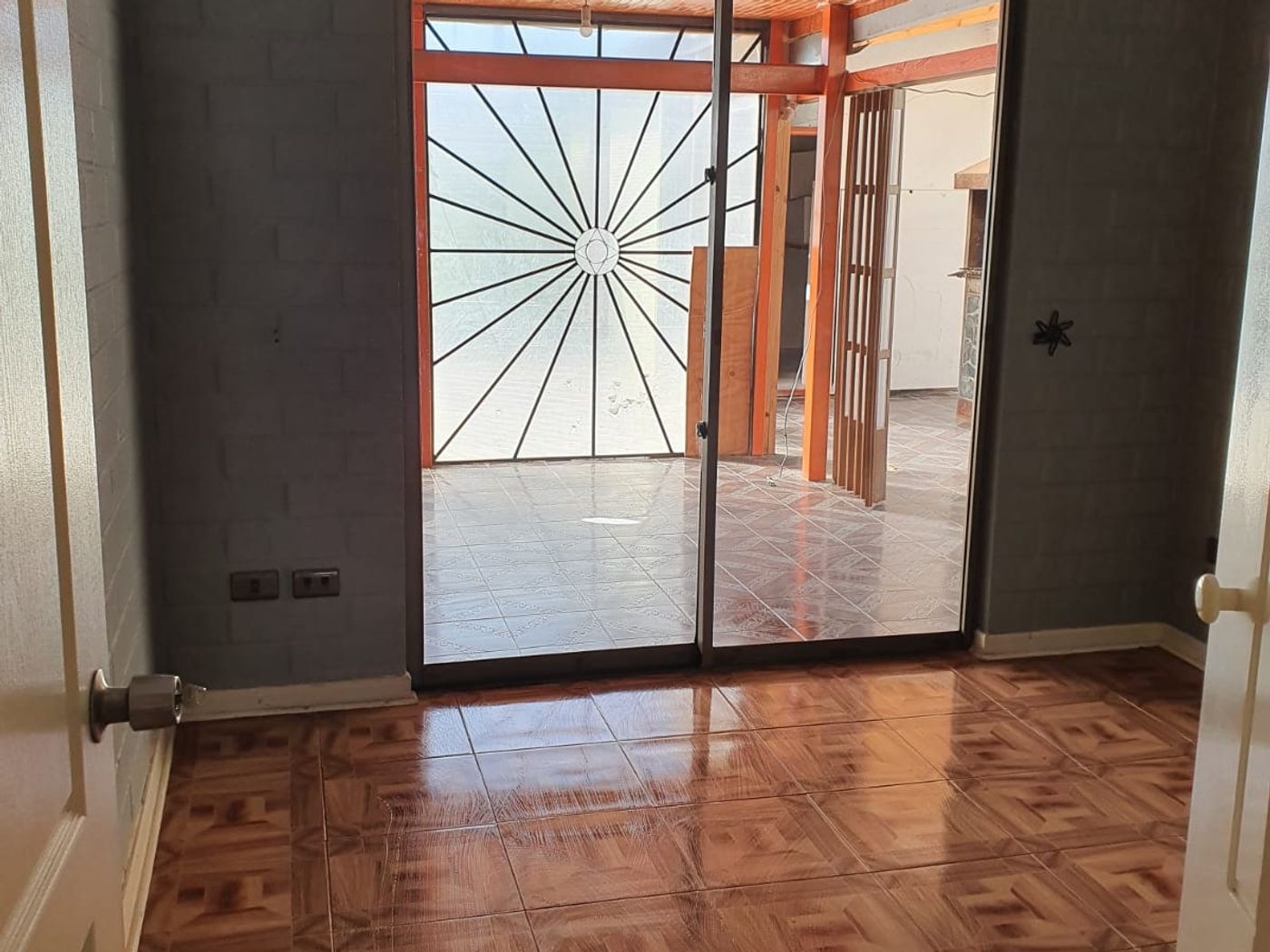 Habitación con piso cerámico diseño parquet y ventanal de acceso al patio con reja metálica.