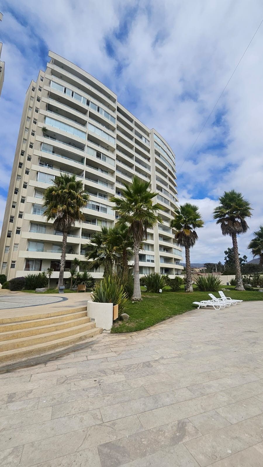 Torre de departamentos con palmeras y explanada de acceso