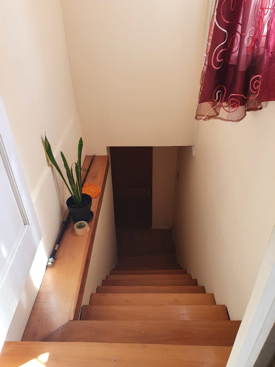 Otra vista del hueco de escalera con cortina roja, maceta y peldaños de madera hacia abajo.