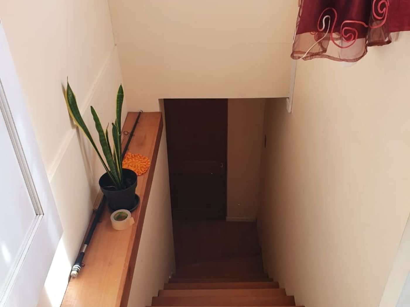 Otra vista del hueco de escalera con cortina roja, maceta y peldaños de madera hacia abajo.
