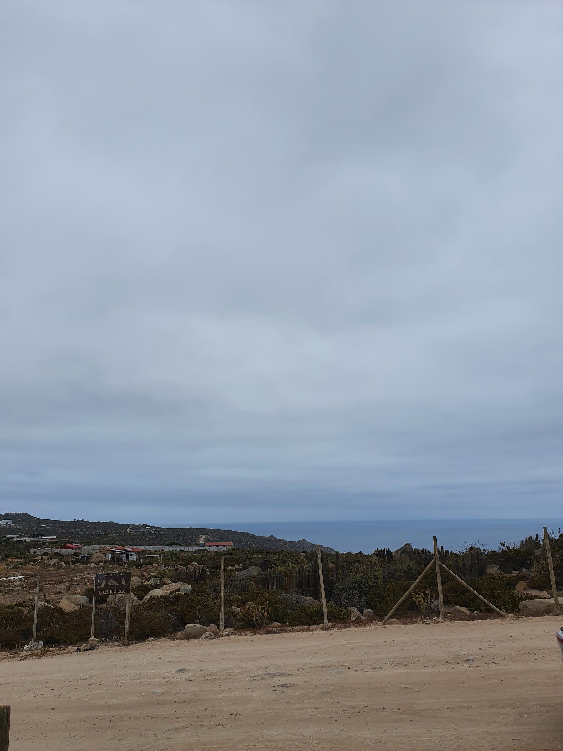 Camino de tierra junto a cerco, mar y cielo nublado