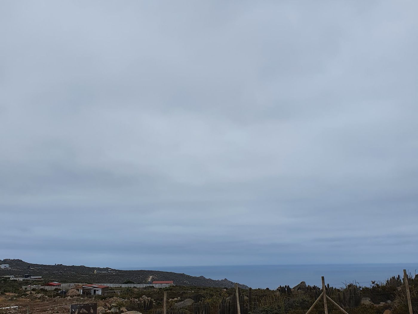 Camino de tierra junto a cerco, mar y cielo nublado