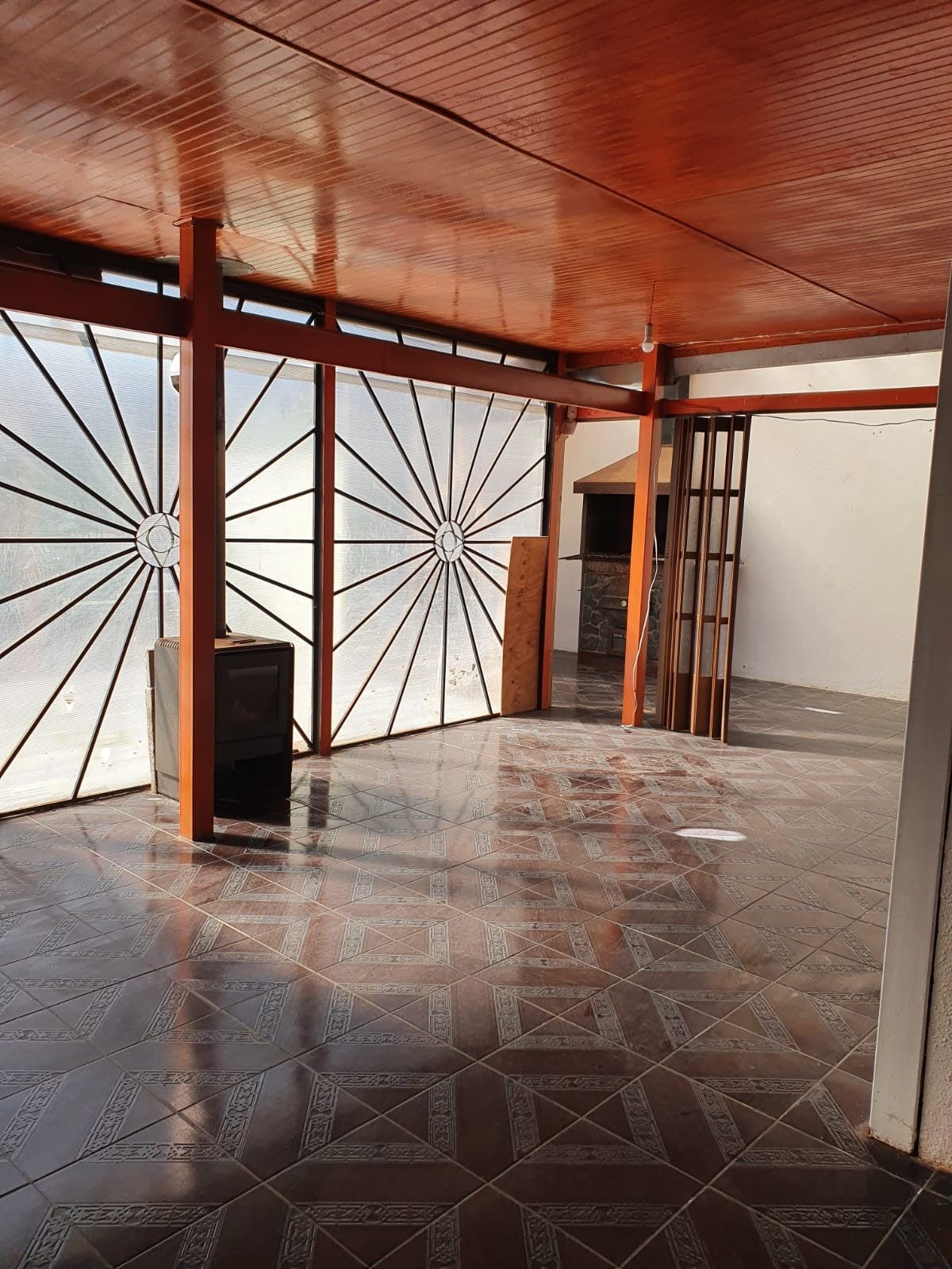 Terraza techada con vigas de madera a la vista, piso cerámico y reja ornamental divisoria.